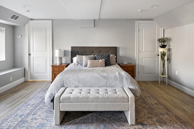 bedroom featuring vaulted ceiling, wood finish floors, visible vents, and baseboards