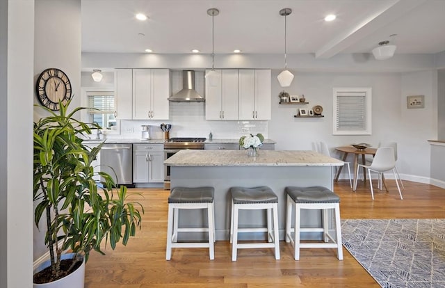 kitchen with stainless steel appliances, a kitchen bar, decorative backsplash, light wood-type flooring, and wall chimney exhaust hood