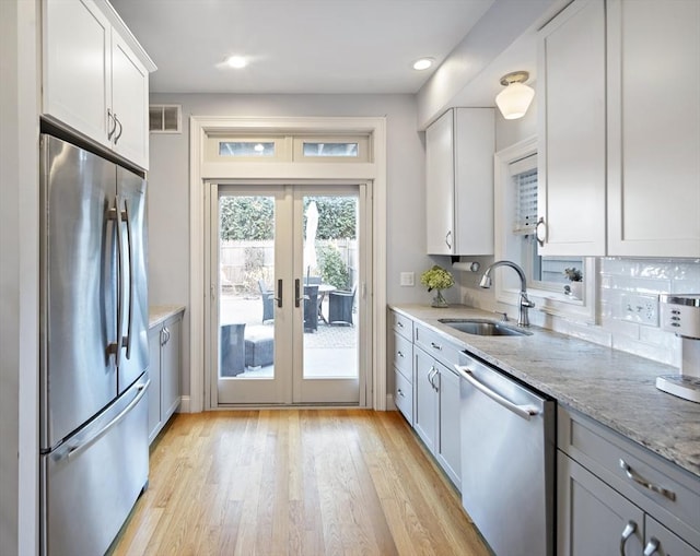 kitchen with light stone counters, french doors, stainless steel appliances, a sink, and light wood-type flooring