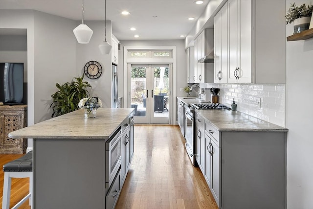 kitchen featuring a breakfast bar area, appliances with stainless steel finishes, french doors, light wood-type flooring, and a sink