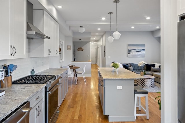 kitchen with a breakfast bar area, open floor plan, stainless steel appliances, light wood-type flooring, and wall chimney range hood