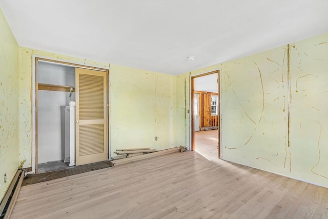 unfurnished bedroom featuring baseboard heating, a closet, and light hardwood / wood-style flooring