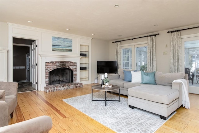 living room featuring a brick fireplace, built in features, and hardwood / wood-style flooring