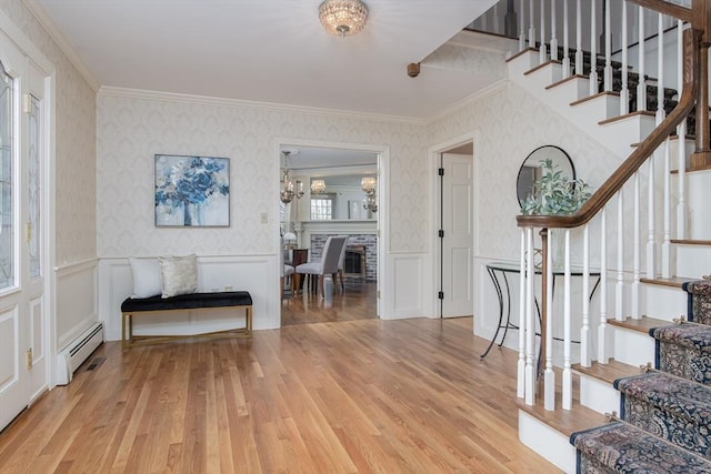 foyer entrance with light hardwood / wood-style flooring, baseboard heating, crown molding, and a notable chandelier