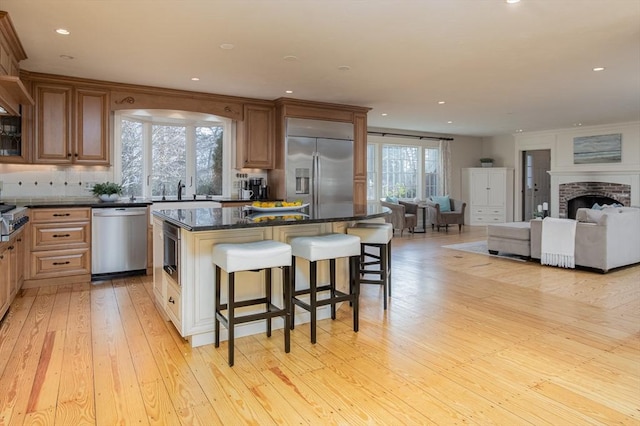 kitchen with a center island, dark stone countertops, light wood-type flooring, a fireplace, and stainless steel appliances