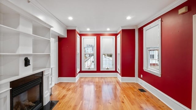 unfurnished living room featuring light wood-type flooring, baseboards, visible vents, and crown molding