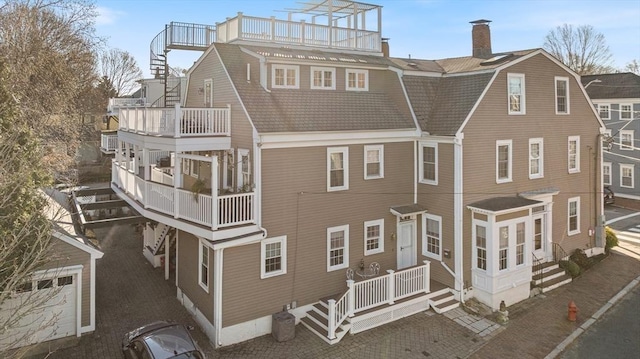 view of front of home with a balcony, a chimney, and a gambrel roof