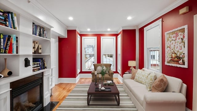 living room with light wood finished floors, a fireplace with flush hearth, a wealth of natural light, and crown molding