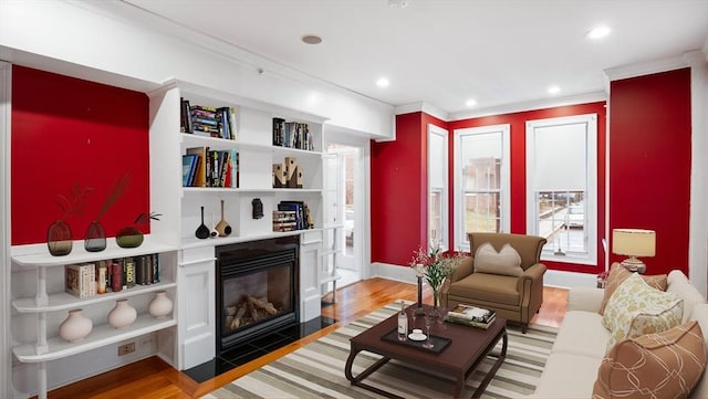 living room featuring ornamental molding, a fireplace with flush hearth, light wood-style flooring, and recessed lighting