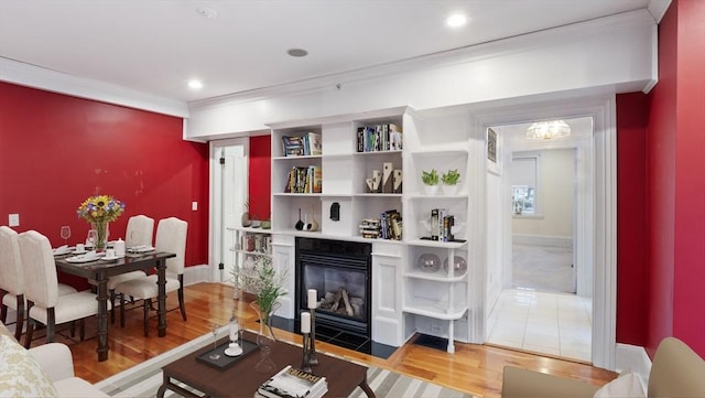 living area featuring recessed lighting, a fireplace with flush hearth, baseboards, light wood-style floors, and ornamental molding