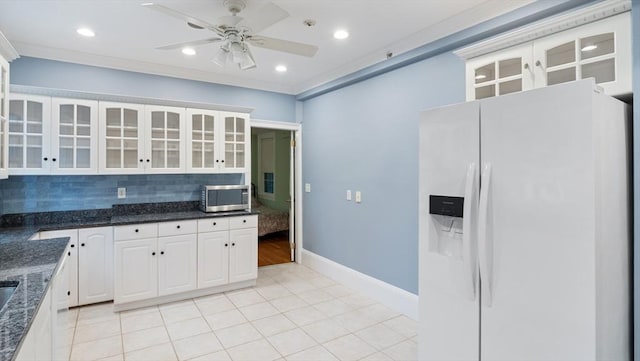 kitchen featuring white refrigerator with ice dispenser, white cabinets, decorative backsplash, stainless steel microwave, and glass insert cabinets