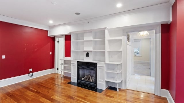 unfurnished living room with light wood-style floors, a fireplace with flush hearth, baseboards, and crown molding