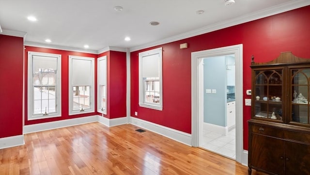 spare room with ornamental molding, visible vents, light wood-style flooring, and baseboards