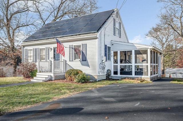 cape cod house featuring a sunroom, a front lawn, and solar panels