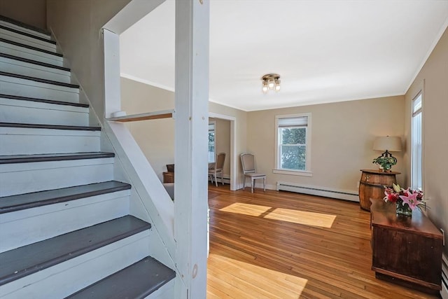 staircase featuring baseboard heating, wood finished floors, and crown molding