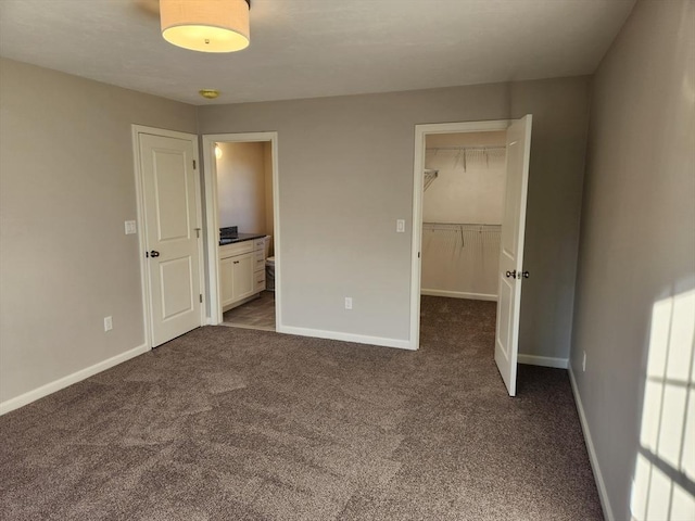 unfurnished bedroom featuring a walk in closet, connected bathroom, a closet, and dark colored carpet