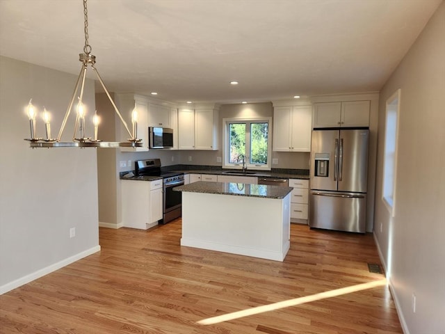 kitchen featuring appliances with stainless steel finishes, hanging light fixtures, light hardwood / wood-style floors, white cabinets, and sink