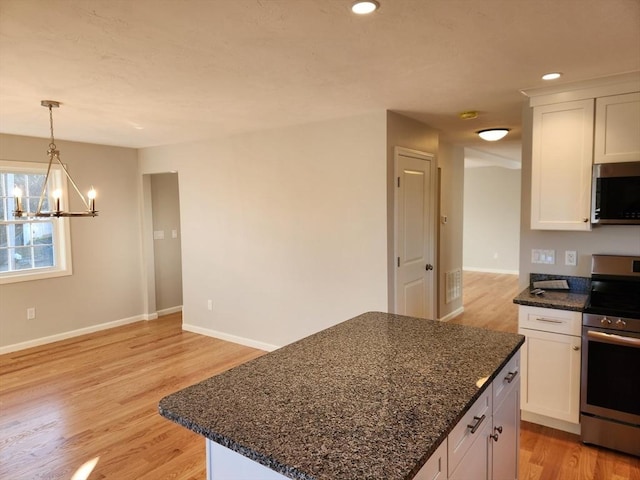 kitchen featuring stainless steel appliances, a kitchen island, an inviting chandelier, white cabinetry, and dark stone countertops