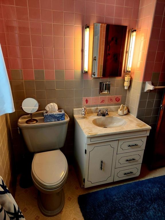 bathroom featuring toilet, vanity, and tile walls