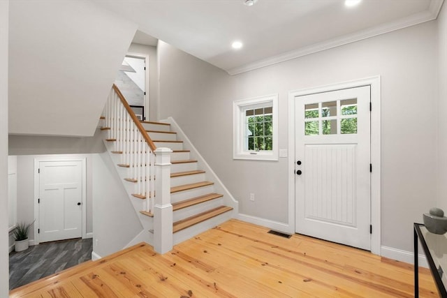 foyer entrance with baseboards, visible vents, stairway, ornamental molding, and wood finished floors