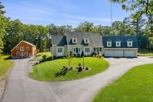 cape cod home with driveway, an attached garage, and a front lawn