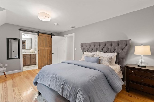 bedroom with light wood-style floors, baseboards, ensuite bathroom, and a barn door