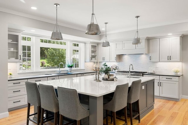 kitchen with glass insert cabinets, light countertops, a kitchen island with sink, and a sink