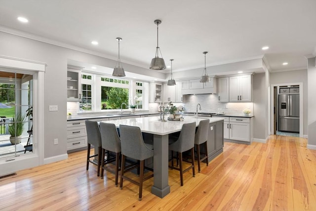 kitchen featuring decorative light fixtures, a breakfast bar, light countertops, stainless steel refrigerator with ice dispenser, and a center island with sink