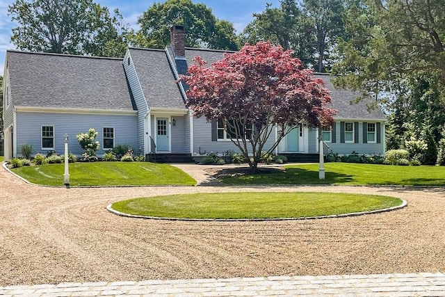 cape cod-style house featuring a shingled roof, a front yard, and a chimney