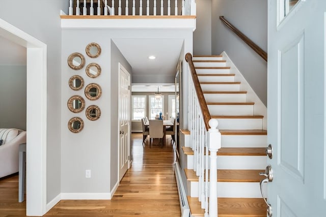 foyer entrance featuring a baseboard heating unit, light wood-type flooring, baseboards, and stairs