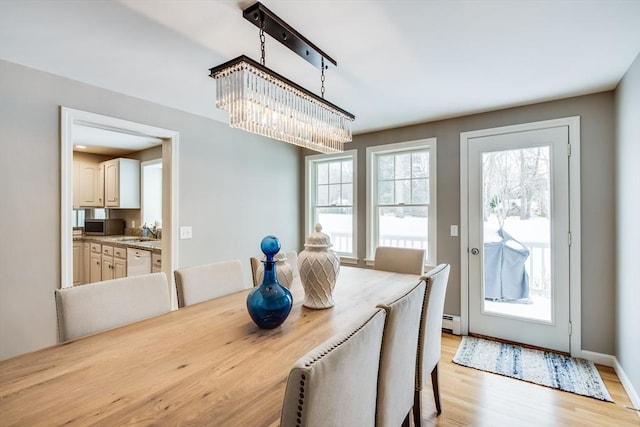 dining space featuring a baseboard heating unit, baseboards, and light wood-style floors