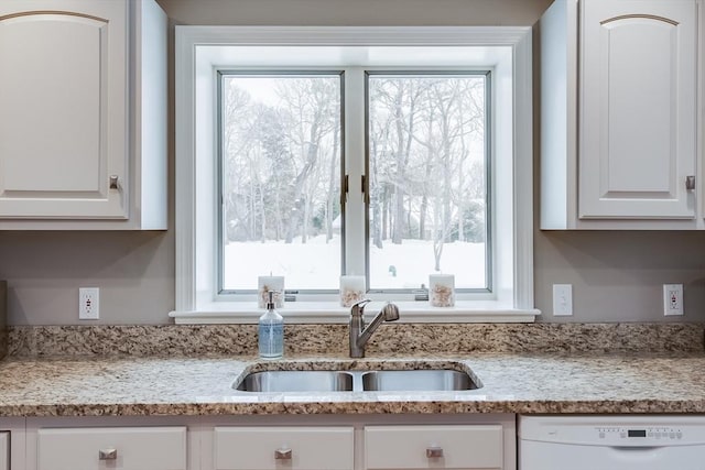 kitchen featuring light stone counters, white dishwasher, a sink, and white cabinetry