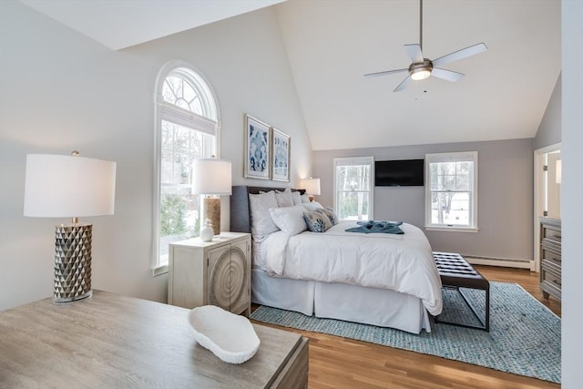 bedroom featuring lofted ceiling, light wood-style flooring, multiple windows, and a baseboard heating unit