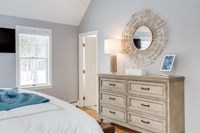 bedroom with light wood finished floors, a baseboard radiator, and vaulted ceiling