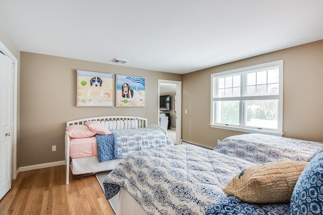 bedroom with light wood-style floors, a baseboard radiator, visible vents, and baseboards