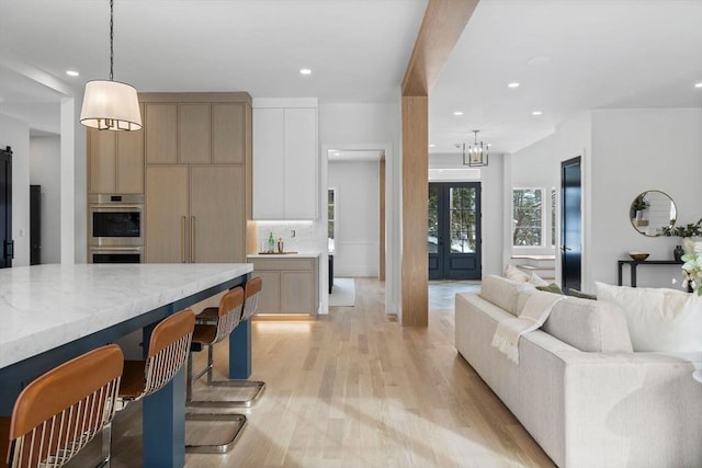 kitchen featuring stainless steel double oven, light hardwood / wood-style floors, decorative backsplash, hanging light fixtures, and light stone counters