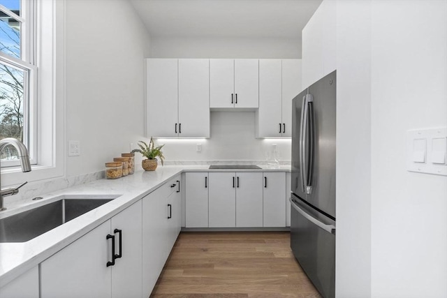 kitchen with white cabinets, a healthy amount of sunlight, light hardwood / wood-style floors, sink, and stainless steel refrigerator