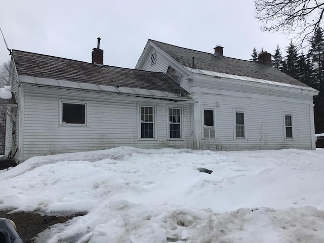 snow covered back of property with a chimney