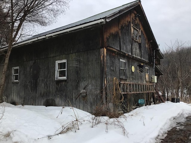 snow covered property with a barn, a detached garage, metal roof, and an outdoor structure