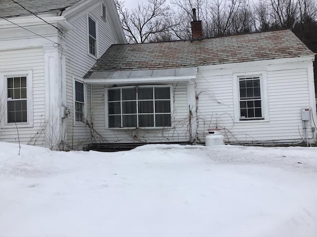 snow covered rear of property featuring a chimney