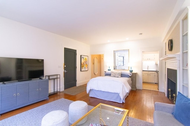 bedroom with baseboards, ensuite bath, a fireplace with flush hearth, hardwood / wood-style floors, and a sink