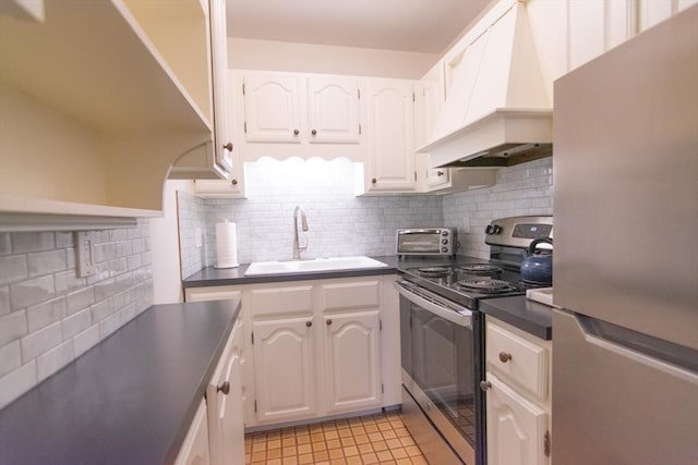 kitchen with custom exhaust hood, stainless steel appliances, dark countertops, white cabinets, and a sink