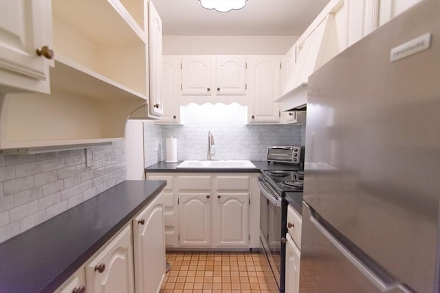 kitchen featuring electric stove, dark countertops, freestanding refrigerator, white cabinetry, and a sink