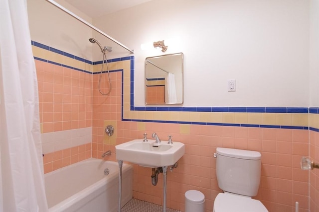 bathroom with tile walls, wainscoting, toilet, shower / bath combination with curtain, and a sink