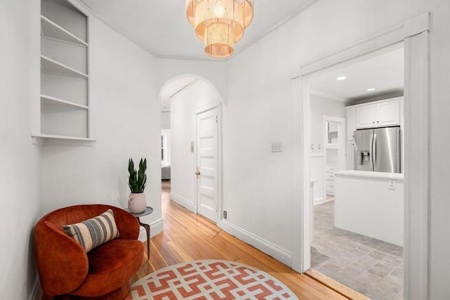 sitting room featuring crown molding, arched walkways, baseboards, and light wood-style flooring