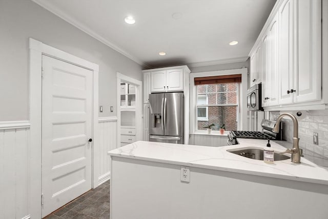 kitchen with crown molding, a peninsula, white cabinets, a sink, and stainless steel appliances