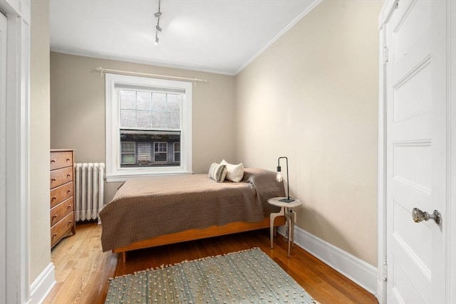bedroom with rail lighting, radiator heating unit, baseboards, wood finished floors, and ornamental molding