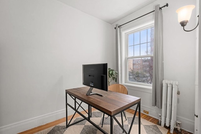 home office featuring baseboards, radiator heating unit, and light wood-type flooring