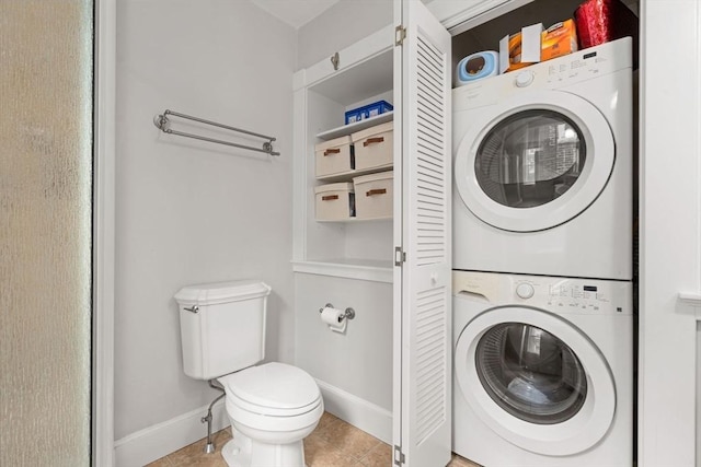 bathroom with toilet, stacked washer / drying machine, baseboards, and tile patterned flooring