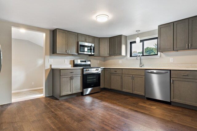 kitchen with appliances with stainless steel finishes, sink, vaulted ceiling, pendant lighting, and dark hardwood / wood-style floors